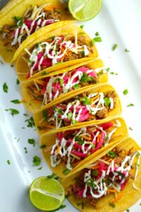 Slow Cooker Pork Tacos with with Pickled Onions, Shredded Cheese, and Cilantro Lime Crema drizzled on top!  It's such an easy dinner since the pork cooks in the slow cooker to be perfectly seasoned and fall apart tender.  #tacos #easydinner #glutenfree #dinner #mexican #pork