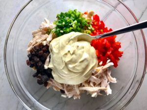 Curry Dressing, shredded chicken, red pepper, scallion, and raisins in bowl for Curry Chicken Salad. It has so many fantastic flavors and textures!  The chicken breast is simply roasted and mixed with a creamy sweet and savory curry dressing.  Red pepper gives you a fresh crunch, scallion gives a savory bite, and raisins give a burst of sweet.  #chicken #chickenrecipes #chickensalad #currychicken #mealprep #lunch #healthyrecipes