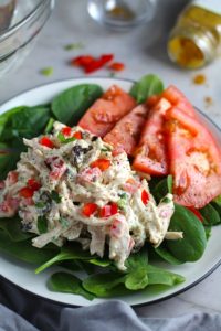 Curry Chicken Salad on spinach with tomato slices. It has so many fantastic flavors and textures!  The chicken breast is simply roasted and mixed with a creamy sweet and savory curry dressing.  Red pepper gives you a fresh crunch, scallion gives a savory bite, and raisins give a burst of sweet.  #chicken #chickenrecipes #chickensalad #currychicken #mealprep #lunch #healthyrecipes
