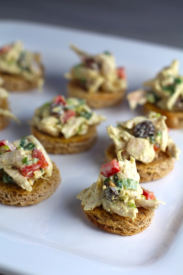 Curry Chicken Salad on toast rouds on plate.  It has so many fantastic flavors and textures!  The chicken breast is simply roasted and mixed with a creamy sweet and savory curry dressing.  Red pepper gives you a fresh crunch, scallion gives a savory bite, and raisins give a burst of sweet.  #chicken #chickenrecipes #chickensalad #currychicken #mealprep #lunch #healthyrecipes