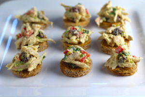 Curry Chicken Salad on toast rouds on plate. It has so many fantastic flavors and textures!  The chicken breast is simply roasted and mixed with a creamy sweet and savory curry dressing.  Red pepper gives you a fresh crunch, scallion gives a savory bite, and raisins give a burst of sweet.  #chicken #chickenrecipes #chickensalad #currychicken #mealprep #lunch #healthyrecipes