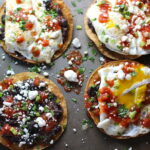 Huevos Tostadas assembled on a sheet pan are utterly delicious! They are similar to the better known Huevos Rancheros but are a pick up and eat with your hands version! They have crispy corn tortillas topped with creamy mashed black beans, a salty fried egg, smoky tomato sauce, cheese, and scallions! #huevosrancheros #eggs #brunch #mexicanrecipes #vegetarian #meatlessrecipes #glutenfree