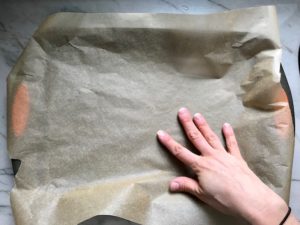 Hand pressing down parchment paper in pan for No Bake Energy Bites. These Easy Nut-Free, No-Bake Energy Bites with Chocolate Chips are magnificent!  They are sweet, chewy, crunchy, & healthy.  Only minutes to make & no Baking! Breakfast, snack, or dessert. #energybars #granolabars #snackrecipes #healthyfood #healthyrecipes #healthysnacks #healthybreakfast #healthydessert
