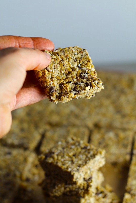 No Bake Energy Bites cut into squares with hand holding one. These Easy Nut-Free, No-Bake Energy Bites with Chocolate Chips are magnificent!  They are sweet, chewy, crunchy, & healthy.  Only minutes to make & no Baking! Breakfast, snack, or dessert. #energybars #granolabars #snackrecipes #healthyfood #healthyrecipes #healthysnacks #healthybreakfast #healthydessert
