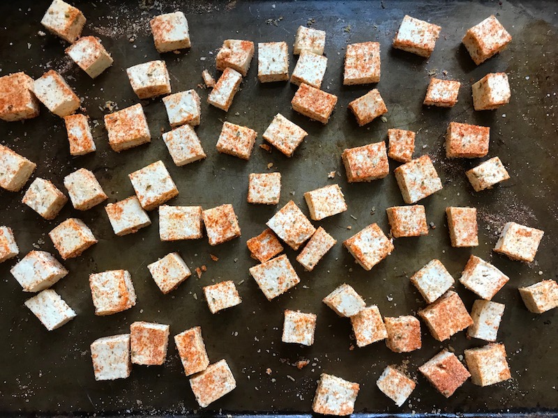Seasoned tofu pieces on pan for Roasted Tofu Croutons. These are seasoned and toasted for the perfect addition to any salad, pasta, rice, or soup!   They get a roasted, almost nutty flavor with a salty and smoky seasoned crust with a chewy bite.  Super easy to make, low carb and great source of protein!  #croutons #salad #tofu #tofurecipes #vegetarian #plantbased #paleo