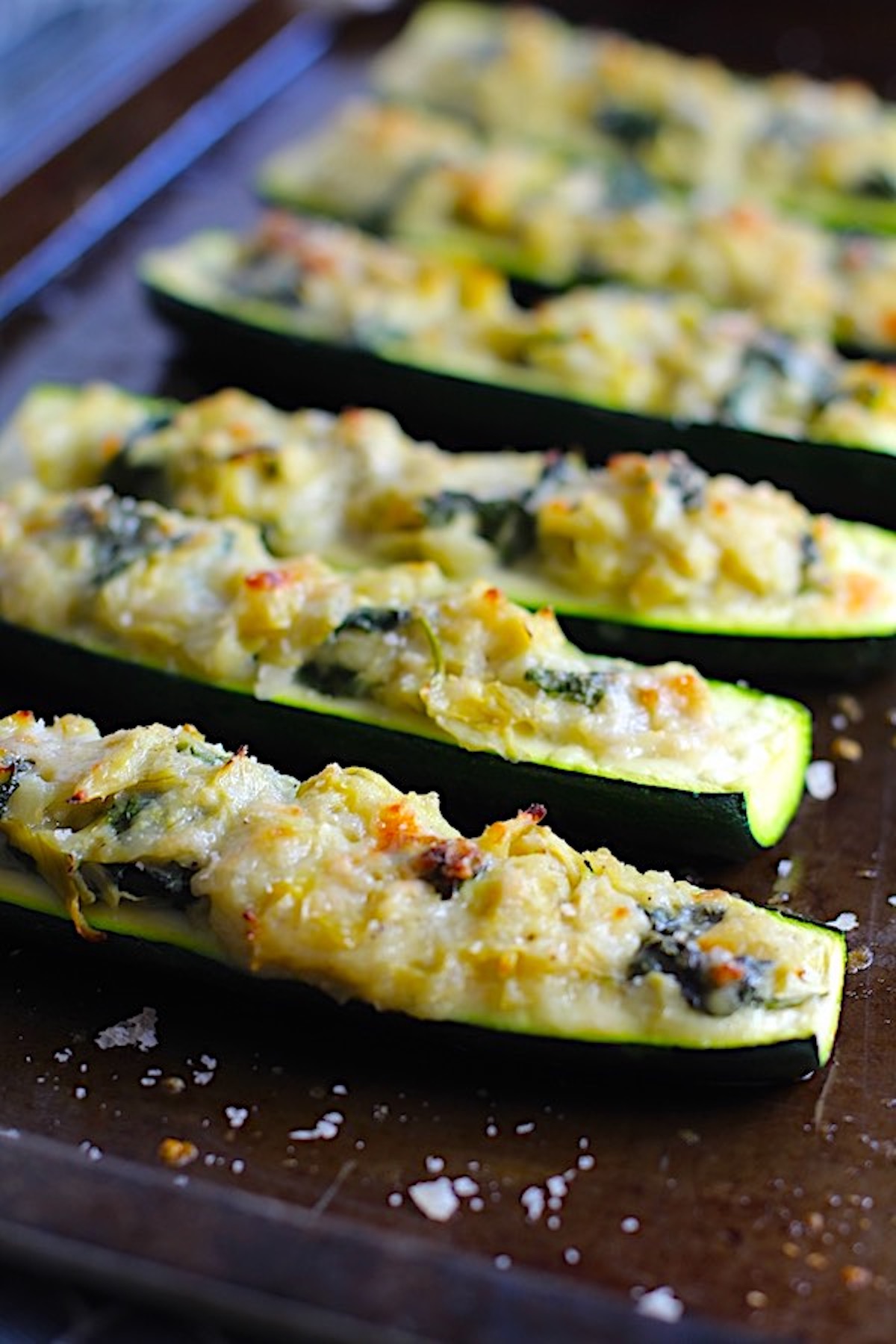 Close up of Artichoke Spinach Stuffed Zucchini Recipe on a pan. Each fantastic bite gives you creamy artichoke, nutty cheesy Parmesan, spinach, and zucchini. Prepare entirely ahead, then bake 20 minutes and enjoy!