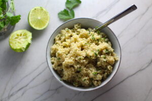 Cilantro Lime Quinoa in a bowl with spoon with lime and cilantro on counter. It's fluffy, nutty, citrusy, salty, and the perfect accompaniment for any protein or vegetable!  With just a few simple ingredients, you can make this fantastic healthier alternative to rice. #quinoa #quinoarecipes #sides #healthyfood