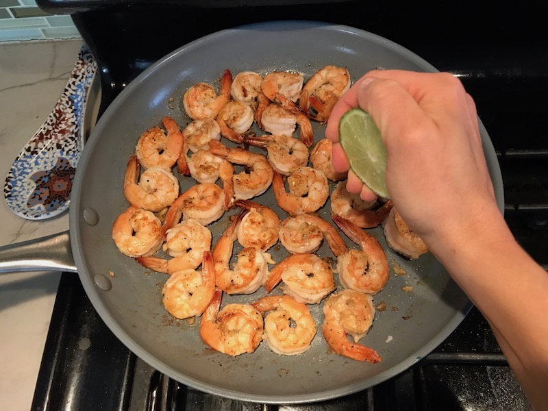 Squeezing lime over cooked shrimp in skillet for Garlic Lime Grilled Greek Shrimp with Tzatziki Sauce.  The Shrimp is simply sauteed with minced garlic, olive oil, and lemon for big bold flavors. The Tzatziki Sauce is bright and cool with creamy yogurt with fresh cucumber, lime, garlic, and scallion. #shrimp #easydinner #dinner #seafoodrecipes #shrimprecipes