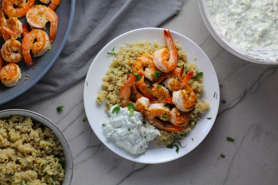 Garlic Lime Pan Grilled Greek Shrimp recipe with Tzatziki Sauce over quinoa on a plate with a pan of shrimp and bowl of quinoa to the left and bowl of tzatziki to the right.