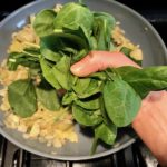 Adding to spinach leaves to onions cooking in pan for Spinach Artichoke Stuffed Zucchini. Each fantastic bite gives you creamy artichoke, nutty cheesy Parmesan, spinach, and zucchini. Prepare entirely ahead, then bake 20 minutes and enjoy! #vegetarian #zucchini #stuffedzuchini #spinach #artichoke #springrecipes #healthyfood #healthydinner #healthyrecipes #glutenfree