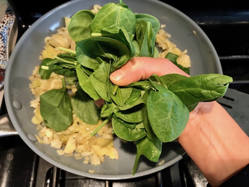 Adding to spinach leaves to onions cooking in pan for  Artichoke Spinach Stuffed Zucchini Recipe. Each fantastic bite gives you creamy artichoke, nutty cheesy Parmesan, spinach, and zucchini. Prepare entirely ahead, then bake 20 minutes and enjoy! #vegetarian #zucchini #stuffedzuchini #spinach #artichoke #springrecipes #healthyfood #healthydinner #healthyrecipes #glutenfree