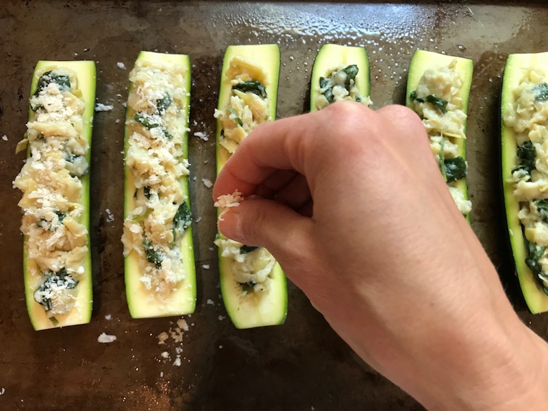 Sprinkling parmesan on stuffed zucchini halves for  Artichoke Spinach Stuffed Zucchini Recipe. Each fantastic bite gives you creamy artichoke, nutty cheesy Parmesan, spinach, and zucchini. Prepare entirely ahead, then bake 20 minutes and enjoy! #vegetarian #zucchini #stuffedzuchini #spinach #artichoke #springrecipes #healthyfood #healthydinner #healthyrecipes #glutenfree