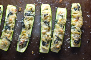Spinach Artichoke Stuffed Zucchini on a pan. Each fantastic bite gives you creamy artichoke, nutty cheesy Parmesan, spinach, and zucchini. Prepare entirely ahead, then bake 20 minutes and enjoy! #vegetarian #zucchini #stuffedzuchini #spinach #artichoke #springrecipes #healthyfood #healthydinner #healthyrecipes #glutenfree