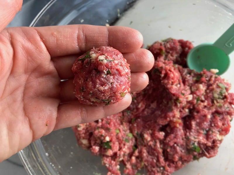 Hand holding a rolled meatball over of raw meatball mixture for Meatballs in Cauliflower Cheese Sauce.