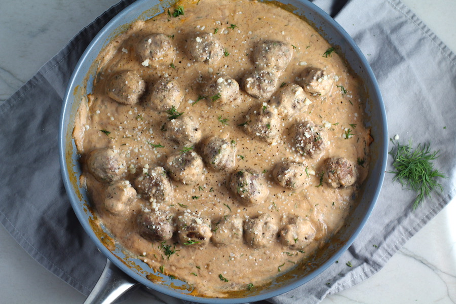 Meatballs in Cauliflower Dill Cream Sauce on plate with fork and skillet in background. The Meatballs are in a creamy cauliflower sauce with garlic, fresh dill, cream cheese, and tomato paste. #meatballs #swedishmeatballs #familydinner #easydinner #dinner #healthydinner
