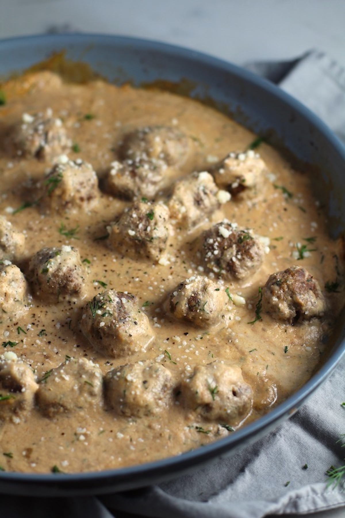 Dill Meatballs in Cauliflower Dill Cream Sauce in a skillet. The Meatballs are swimming in a beautiful creamy cauliflower sauce flavored with garlic, fresh dill, cream cheese, and a touch of tomato paste. 