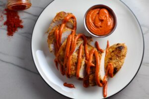 Hungarian Paprika Chicken sliced on plate with Paprika Aioli drizzled on top and fork dipping a bite. The paprika gives beautiful color and a deep, peppery flavor. #chicken #easychicken #easydinner #dinner #healthydinner