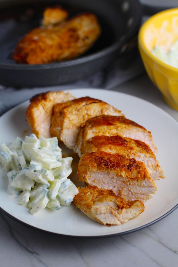 Hungarian Paprika Chicken sliced on plate with Cucumber Salad on the side. The paprika gives beautiful color and a deep, peppery flavor. #chicken #easychicken #easydinner #dinner #healthydinner