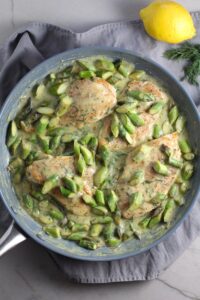 Cooked Lemon Dill Sauce Chicken and Asparagus in pan on stove. It has chicken in a light and creamy sauce flavored with garlic, lemon and fresh dill. It's loaded with fresh asparagus. #springrecipes #dinner #easydinner #healthydinner #lemon #asparagus #chicken #glutenfree #easyrecipes