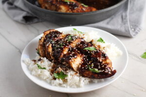 Sesame Sweet Chili Chicken cooked and sliced on a plate with rice and cilantro. It is slightly sweet, tangy, savory, nutty, with a touch of heat. You can prepare it days ahead, it takes just minutes to prepare, minutes to cook, and everyone will love it!! #chicken #marinades #easydinner #easychicken #chickenrecipes #easysauces #healthydinner #healthyfood #healthyrecipes