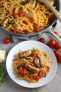 Chicken and Cherry Tomato Pasta with basil and parmesan on a plate with skillet in back. It's easy and so delicious! #pasta #tomatoes #easydinner #dinner #easyrecipes #healthydinner #chicken