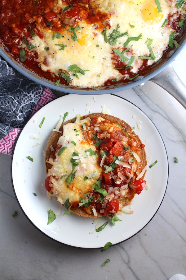 Skillet Eggs in Spicy Tomato Pepper Sauce with Manchego Cheese served over a crispy corn tortilla with skillet in back. With a smoky, spicy, thick, and luscious red pepper tomato sauce. #eggs #huevosrancheros #tomatosauce #easydinner #brunch #shakshuka