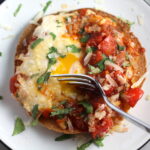 Skillet Eggs in Spicy Tomato Pepper Sauce with Manchego Cheese served over a crispy corn tortilla with skillet in back. With a smoky, spicy, thick, and luscious red pepper tomato sauce. #eggs #huevosrancheros #tomatosauce #easydinner #brunch #shakshuka