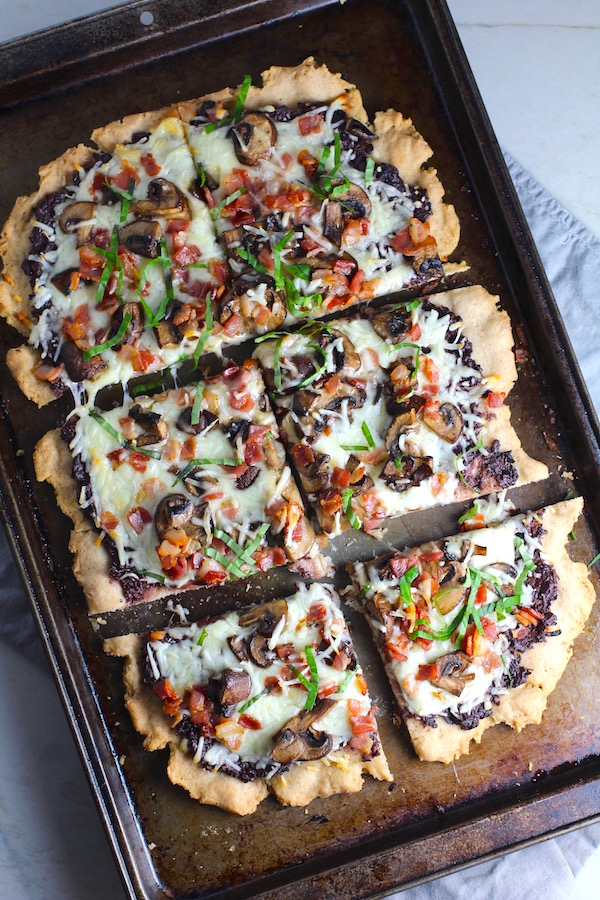 Flatbread cut into 3 pieces on a pan with a crispy gluten free crust, salty and briny Olive Tapenade,  creamy mozzarella, earthy and meaty mushrooms, peppery pancetta, and fresh basil.  #flatbread #pizza #olives #tapenade #mediterranean #easydinner #dinner