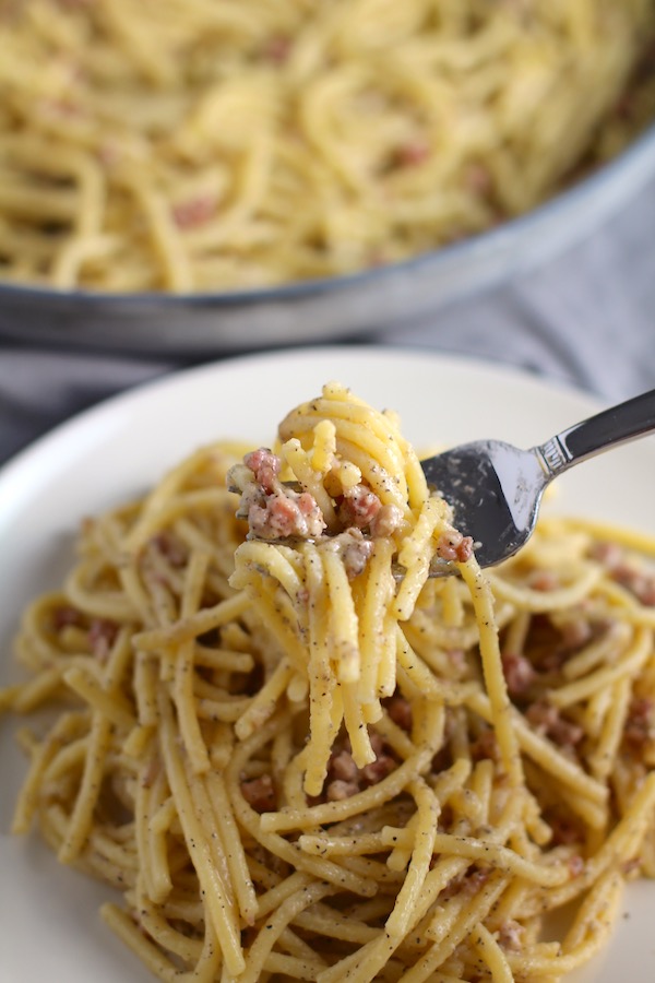 Pancetta, Parmesan, and Pepper Pasta on plate with fork holding bite. The Pancetta gives a salty and slightly peppery flavor, Parmesan cheese creates a nutty and creamy sauce, and the ground black pepper gives a peppery flavor that makes this pasta stand out. #pasta #easypasta #easydinner #dinner #italian #familydinner #onpotdinners #onepandinners #parmesan