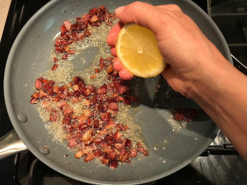 Hand squeezing half a lemon over cooked diced Pancetta in skillet for Pancetta, Parmesan, and Pepper Pasta. The Pancetta gives a salty and slightly peppery flavor, Parmesan cheese creates a nutty and creamy sauce, and the ground black pepper gives a peppery flavor that makes this pasta stand out. #pasta #easypasta #easydinner #dinner #italian #familydinner #onpotdinners #onepandinners #parmesan