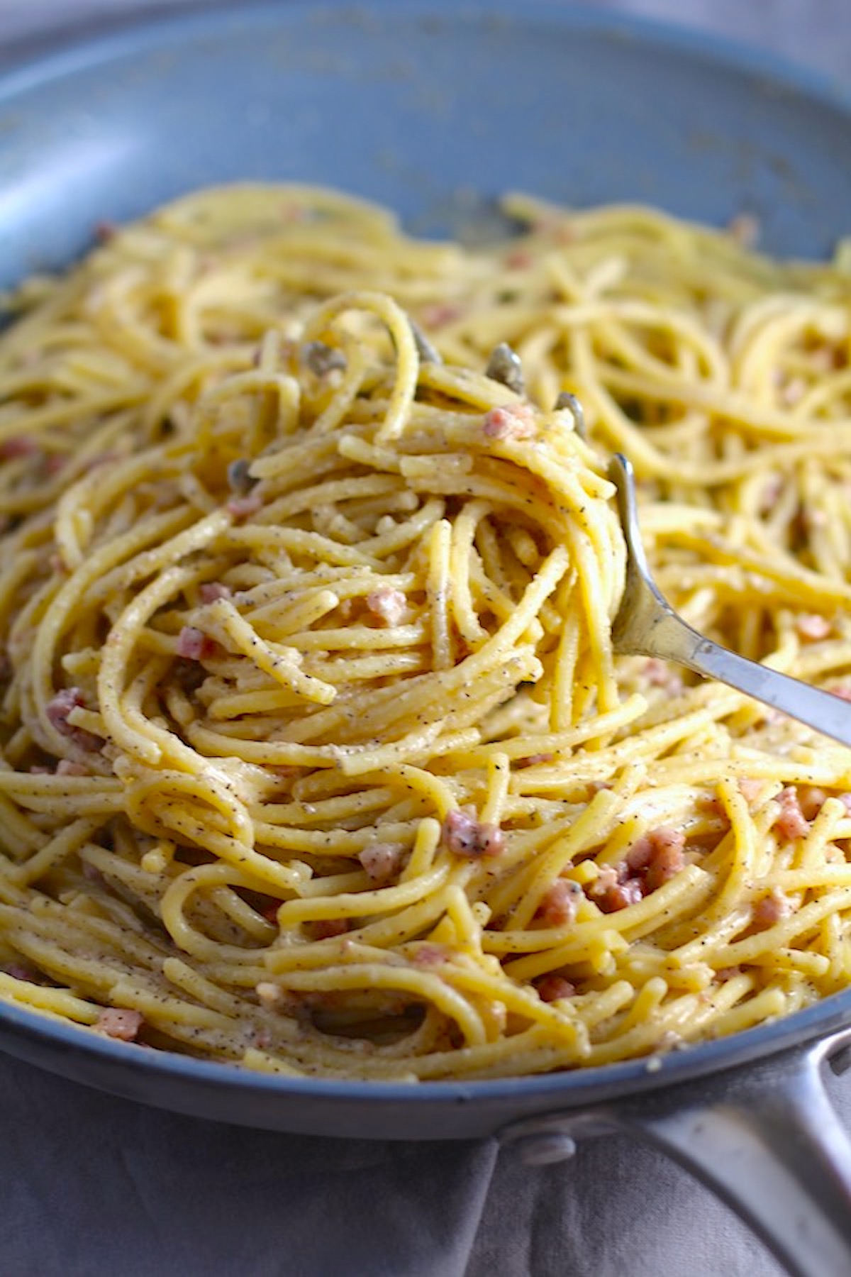 Pasta with Pancetta Parmesan and Black Pepper in skillet with a spoon. The Pancetta gives a salty and slightly peppery flavor, Parmesan cheese creates a nutty and creamy sauce, and the ground black pepper gives a peppery flavor that makes this pasta stand out. #pasta #easypasta #easydinner #dinner #italian #familydinner #onpotdinners #onepandinners #parmesan