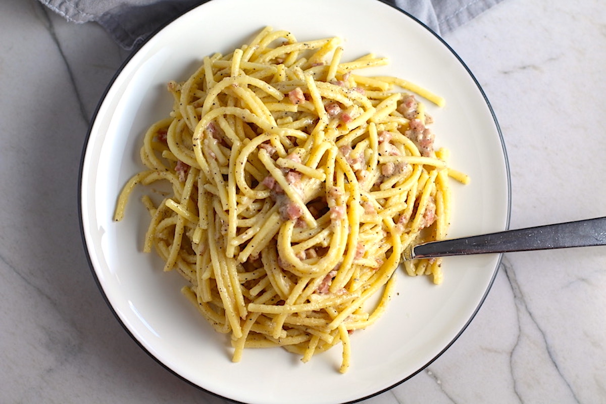Pasta with Pancetta Parmesan and Black Pepper on a plate with a fork full of pasta. The Pancetta gives a salty and slightly peppery flavor, Parmesan cheese creates a nutty and creamy sauce, and the ground black pepper gives a peppery flavor that makes this pasta stand out.
