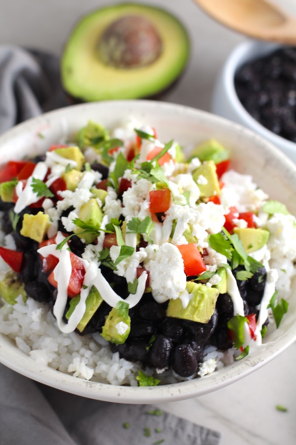 Black Bean Taco Bowl with rice, smoky black beans, avocado, salty Cotija cheese, sour cream, fresh tomato, and bright cilantro.  This Black Bean Taco Bowl Bar lets everyone fills their bowl with any of the toppings they want!  Perfect for kids.  #tacos #tacobowls #healthyfood  #dinner #healthydinner #familydinner #kidsdinner #blackbeans #vegetarian