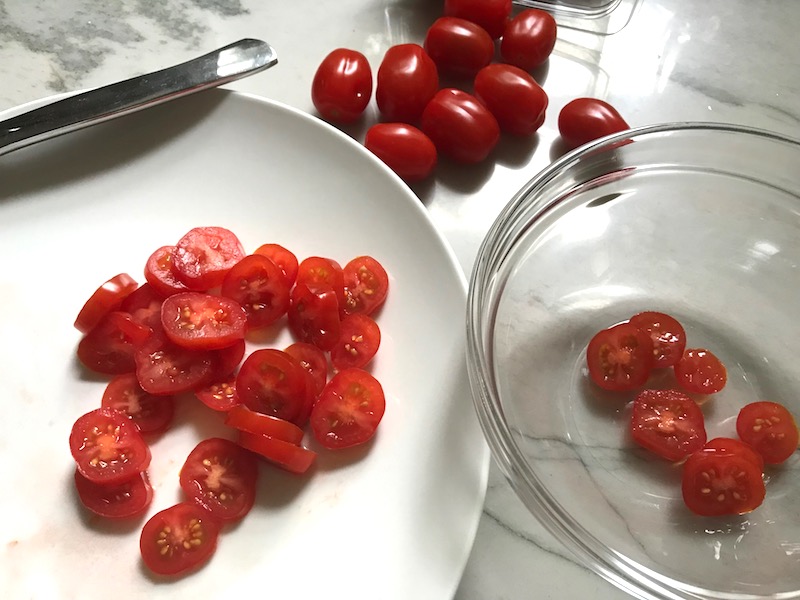 Sliced grape tomatoes for Grilled Halloumi Cheese & Tomato Salad. It's insanely delicious! Grilled Halloumi has a strong savory and salty flavor that is slightly creamy and incredibly addictive. Paired with my simple Tomato and Basil salad, each bite is simply heaven. #halloumi #appetizers #salads #grilling #summerfood