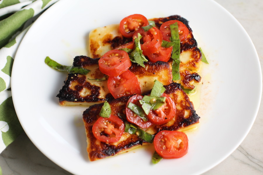 Grilled Halloumi Cheese & Tomato Salad on plate. It's insanely delicious! Grilled Halloumi has a strong savory and salty flavor that is slightly creamy and incredibly addictive. Paired with my simple Tomato and Basil salad, each bite is simply heaven. #halloumi #appetizers #salads #grilling #summerfood