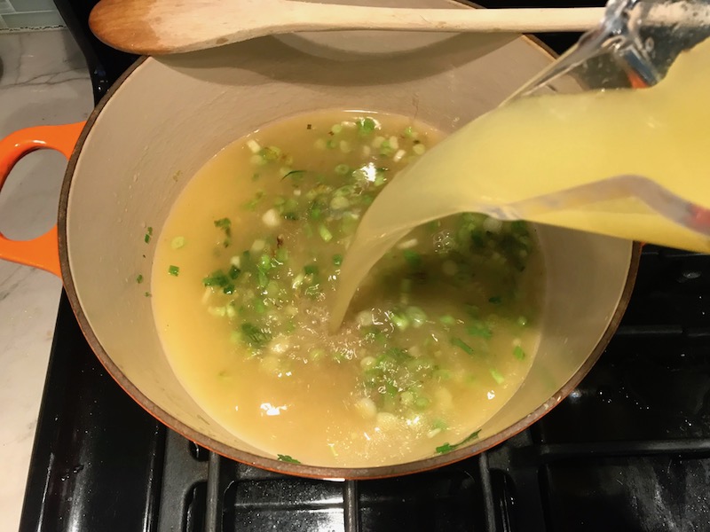 Pouring broth over sliced scallions in a soup pot for Chilled Golden Corn Soup with Turmeric. Scallions on top for garnish. It's thick, creamy, silky and delicious.  The entire family will love this easy stovetop corn soup! #summerfood #cornsoup #corn #vegetarian #vegetablerecipes #sides