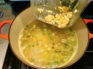 Adding corn kernels to scallions and broth in pot for Chilled Golden Corn Soup with Turmeric.  Scallions on top for garnish. It's thick, creamy, silky and delicious.  The entire family will love this easy stovetop corn soup! #summerfood #cornsoup #corn #vegetarian #vegetablerecipes #sides