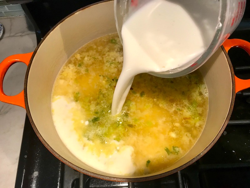 Adding Cornstarch slurry to corn soup in pot for Chilled Golden Corn Soup with Turmeric. Scallions on top for garnish. It's thick, creamy, silky and delicious.  The entire family will love this easy stovetop corn soup! #summerfood #cornsoup #corn #vegetarian #vegetablerecipes #sides