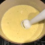 Immersion blender blending corn soup in pot for Chilled Golden Corn Soup with Turmeric. Scallions on top for garnish. It's thick, creamy, silky and delicious.  The entire family will love this easy stovetop corn soup! #summerfood #cornsoup #corn #vegetarian #vegetablerecipes #sides