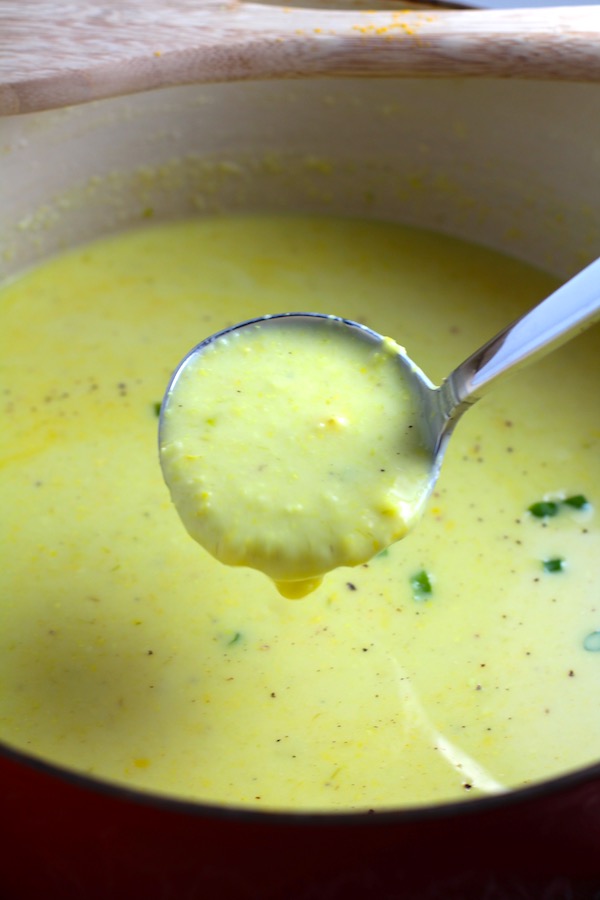 Closeup of Chilled Golden Corn Soup in a pot with a ladle scooping soup up. Scallions on top for garnish. It's thick, creamy, silky and delicious.  The entire family will love this easy stovetop corn soup! #summerfood #cornsoup #corn #vegetarian #vegetablerecipes #sides