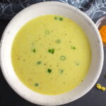 Chilled Golden Corn Soup in a bowl with turmeric spice in a bowl on the side. Scallions on top for garnish. It's thick, creamy, silky and delicious. The entire family will love this easy stovetop corn soup! #summerfood #cornsoup #corn #vegetarian #vegetablerecipes #sides