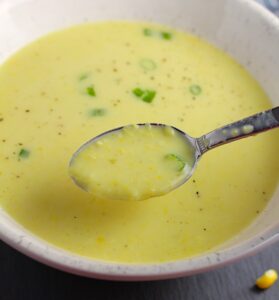 Closeup of Chilled Golden Corn Soup in a bowl with a spoon in it. Scallions on top for garnish. It's thick, creamy, silky and delicious.  The entire family will love this easy stovetop corn soup! #summerfood #cornsoup #corn #vegetarian #vegetablerecipes #sides