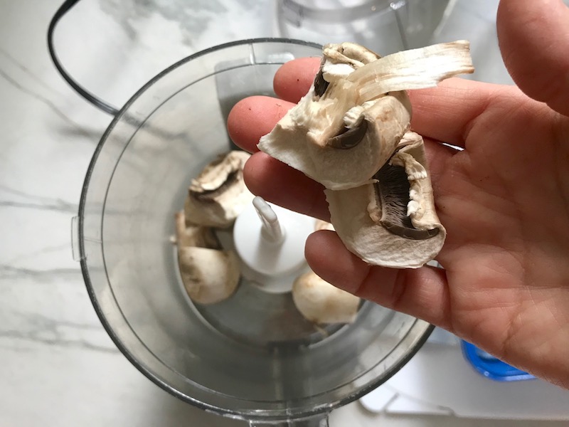 Hand dropping mushrooms into processor for Thick & Creamy Healthy Mushroom Soup. The soup has earthy mushrooms, aeromatic onions, flavorful oregano, and bright chives. 
