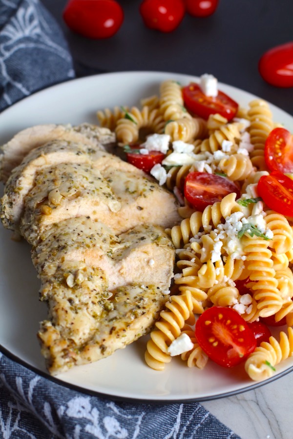 Mediterranean Chicken sliced on plate with a tomato and feta pasta. This Mediterranean Marinade is only a few ingredients, can be made ahead, and is delicious!
