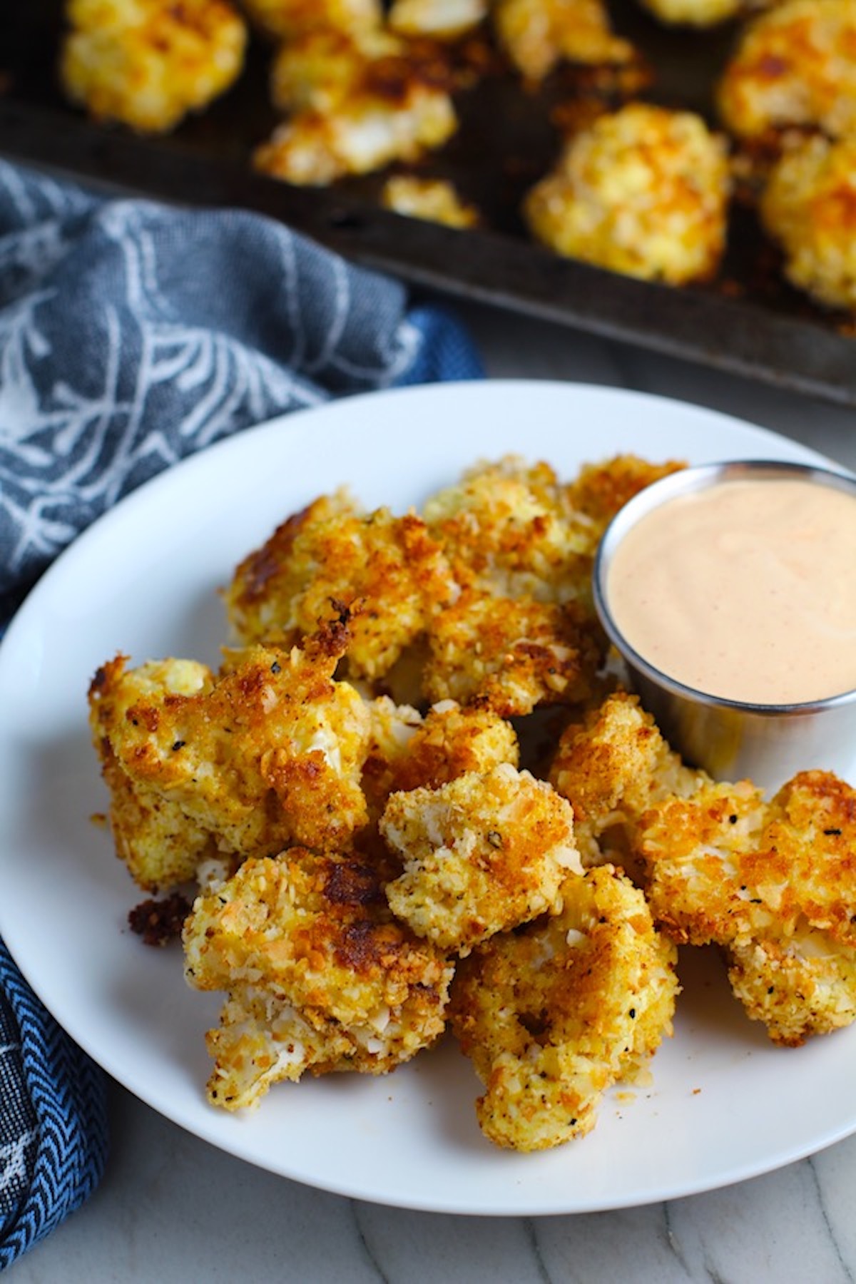 Baked Breaded Cauliflower Recipe on plate with Sriracha Mayo dipping sauce.  They have a slightly sweet and salty crunch outside from the shredded coconut and panko mixture.  The inside is soft and creamy.  Dip in the Sriracha Mayo. 