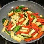 Red Peppers and Zucchini in pan for Family Coconut Curry. The sauce has onion, coconut milk, ginger, garlic, and warm Indian Curry spices.