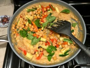 Chickpea Coconut Curry in pan with red peppers, zucchini, and roasted chickpeas. The sauce has onion, coconut milk, ginger, garlic, and warm Indian Curry spices.