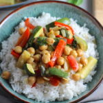 Family Zucchini Chickpea Curry over rice in a bowl with red bell pepper, zucchini, onion, coconut milk, and warm Indian Curry spices.