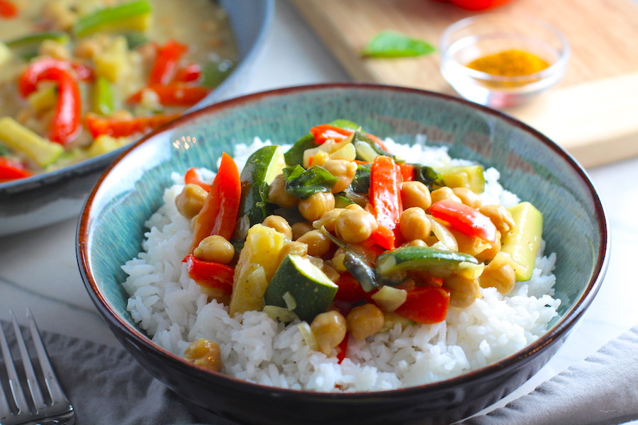 Family Zucchini Chickpea Curry over rice in a bowl with red bell pepper, zucchini, onion, coconut milk, and warm Indian Curry spices.