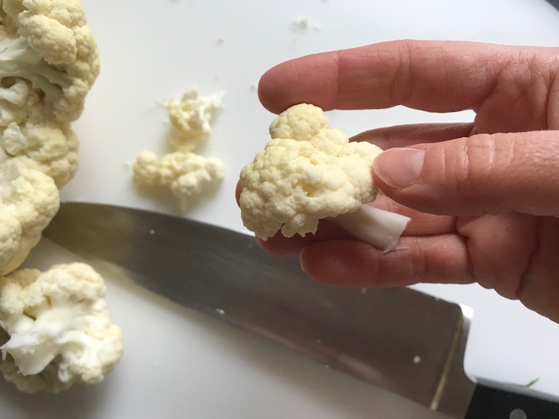 Knife cutting cauliflower for Baked Coconut Cauliflower Bites.  They have a slightly sweet and salty crunch outside from the shredded coconut and panko mixture.  The inside is soft and creamy.  Dip in the Sriracha Mayo.  Baked, not fried, so healthy!  Easy to make, easy to eat! #cauliflowerrecipes #healthyrecipes #sidedishes #appetizers #healthysnacks